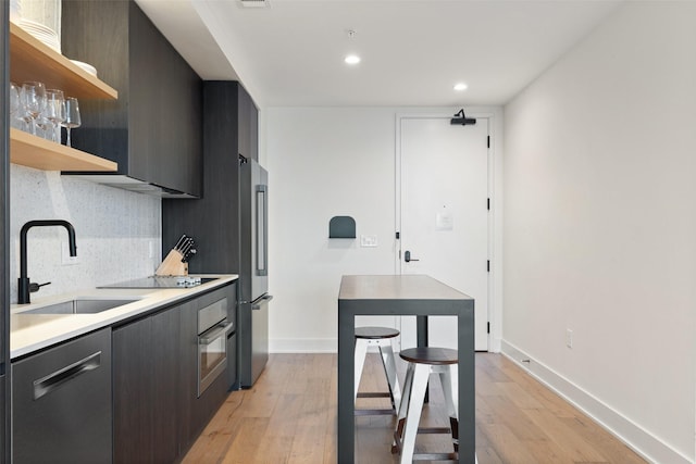 kitchen with sink, light wood-type flooring, a kitchen breakfast bar, stainless steel appliances, and backsplash