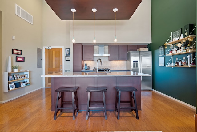 kitchen featuring wall chimney range hood, sink, hanging light fixtures, tasteful backsplash, and high end refrigerator