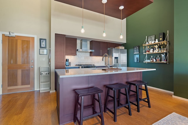 kitchen with sink, stainless steel fridge, a kitchen breakfast bar, decorative backsplash, and wall chimney exhaust hood