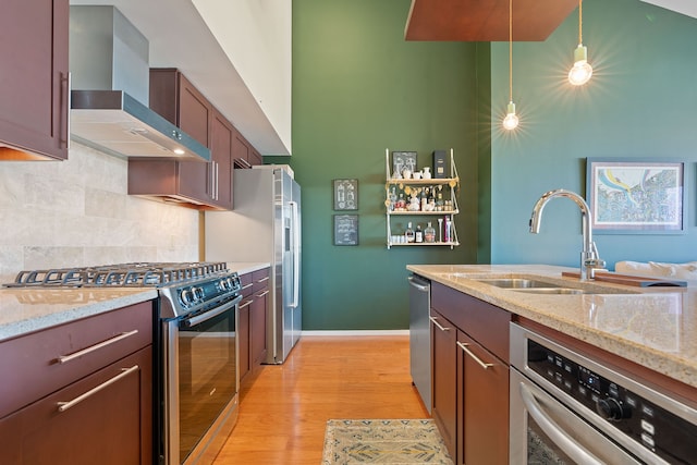 kitchen featuring wall chimney range hood, stainless steel appliances, tasteful backsplash, light stone countertops, and decorative light fixtures