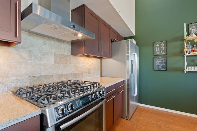 kitchen with backsplash, appliances with stainless steel finishes, wall chimney exhaust hood, and light wood-type flooring