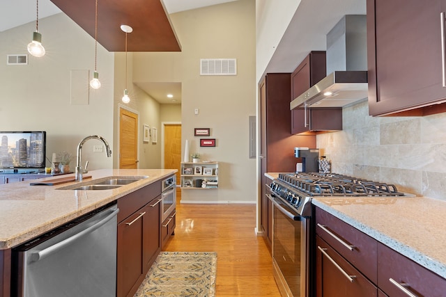 kitchen with decorative light fixtures, sink, light stone counters, stainless steel appliances, and wall chimney range hood