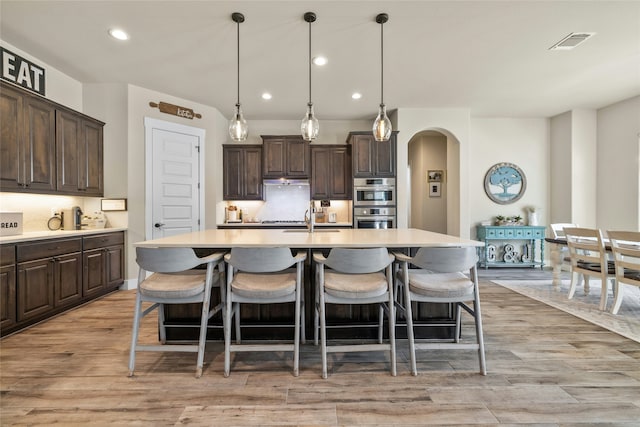 kitchen with pendant lighting, dark brown cabinets, a center island with sink, and light hardwood / wood-style flooring