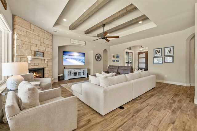 living room featuring beamed ceiling, ceiling fan, a stone fireplace, and light hardwood / wood-style flooring