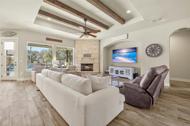 living room featuring beam ceiling, a stone fireplace, and ceiling fan