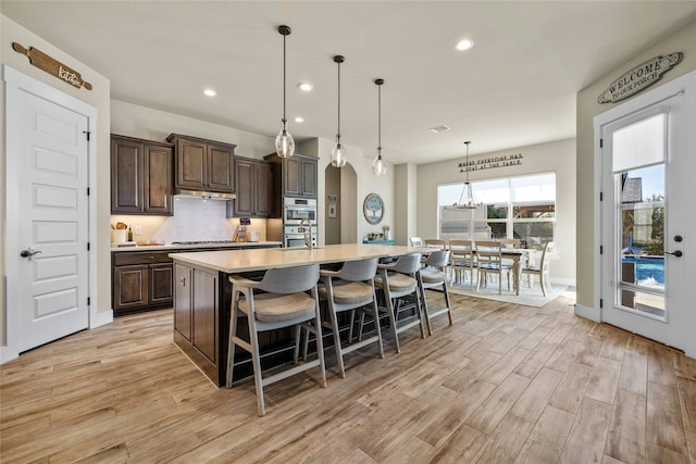 kitchen with stainless steel gas stovetop, a breakfast bar area, dark brown cabinets, light wood-type flooring, and a spacious island