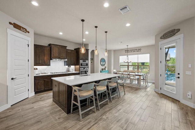 105 Aldea St, Georgetown, TX 78633 - kitchen with light countertops, light wood finished floors, dark brown cabinetry, recessed lighting, and an island with sink