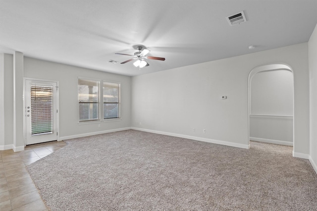 empty room with baseboards, visible vents, arched walkways, a ceiling fan, and light tile patterned flooring