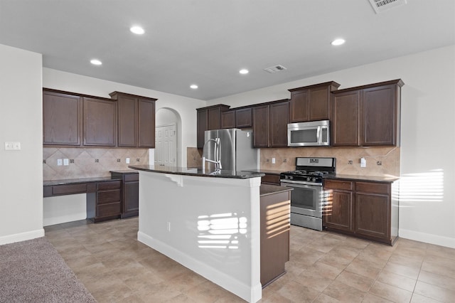 kitchen featuring dark brown cabinetry, a center island with sink, visible vents, arched walkways, and stainless steel appliances