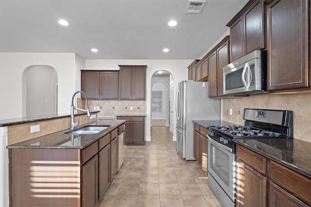 kitchen with visible vents, arched walkways, dark stone counters, appliances with stainless steel finishes, and a sink