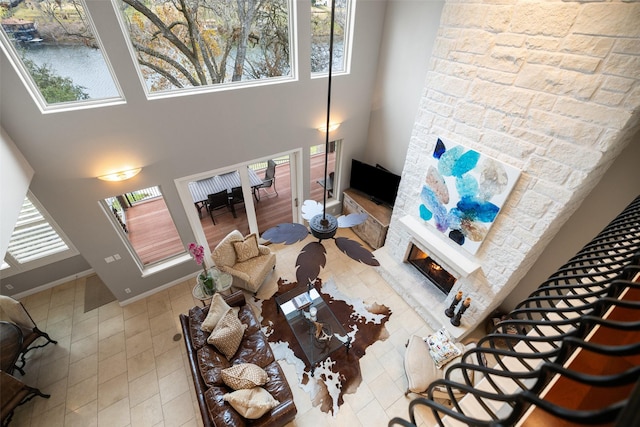 living room featuring a stone fireplace, plenty of natural light, and a high ceiling