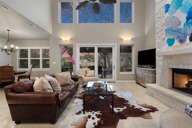 living room with a towering ceiling, a fireplace, ceiling fan with notable chandelier, and light tile patterned floors