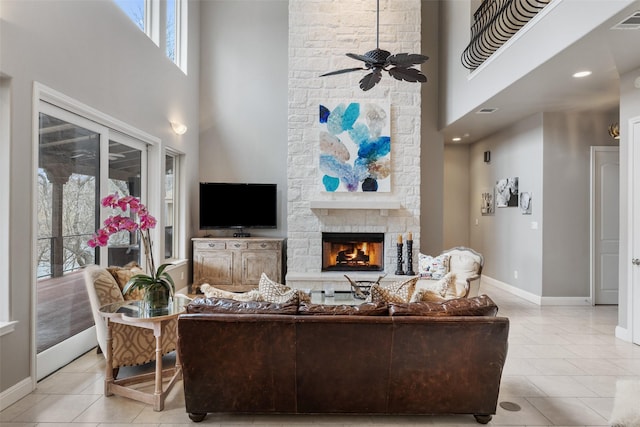 living room featuring ceiling fan, a towering ceiling, a stone fireplace, and light tile patterned flooring