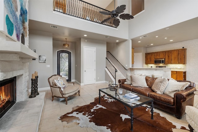 tiled living room featuring ceiling fan, a towering ceiling, and a fireplace