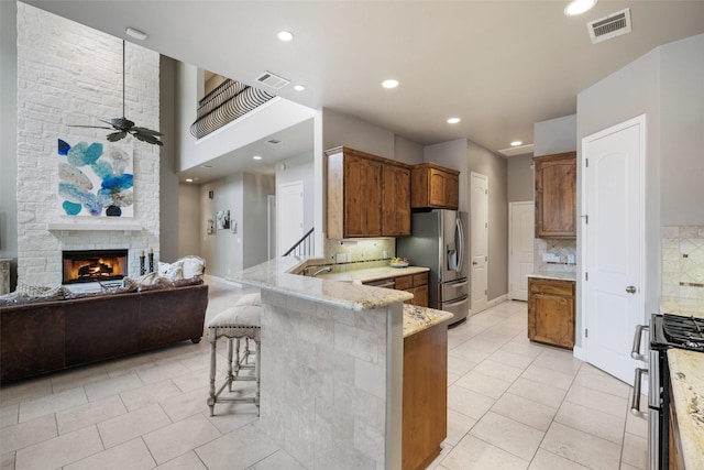 kitchen with a breakfast bar area, ceiling fan, stainless steel appliances, a fireplace, and decorative backsplash