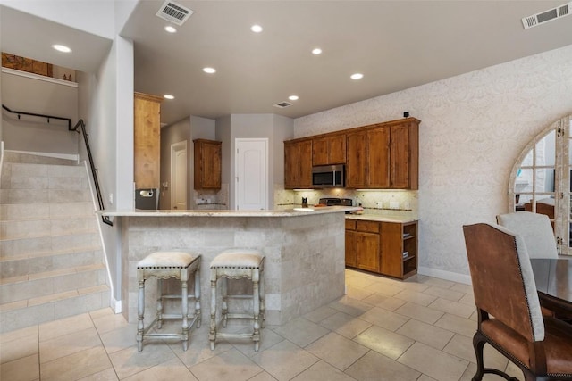 2007 Big Horn Dr, Austin, TX 78734 - kitchen featuring stainless steel microwave, recessed lighting, light countertops, brown cabinetry, and a kitchen bar