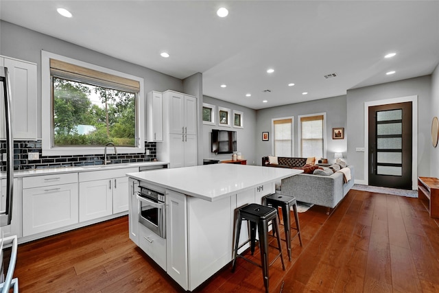 kitchen featuring a breakfast bar, sink, white cabinetry, stainless steel oven, and a center island