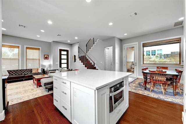 kitchen with white cabinetry, a center island, oven, and dark wood-type flooring