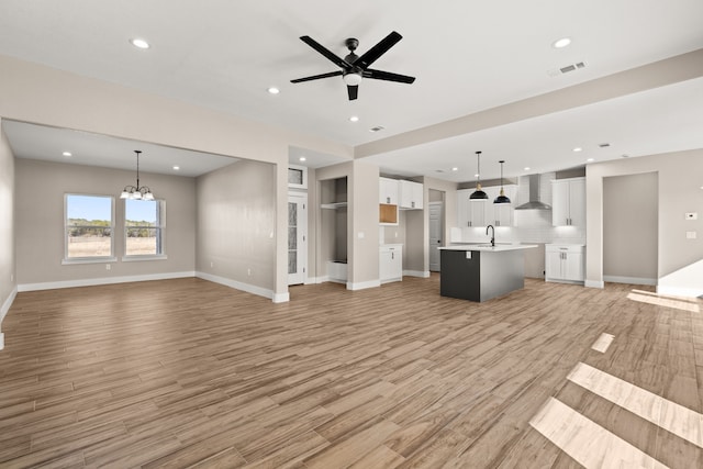 unfurnished living room featuring sink, ceiling fan with notable chandelier, and light wood-type flooring