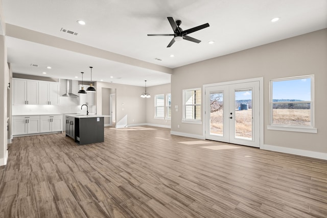 unfurnished living room featuring sink, ceiling fan with notable chandelier, light wood-type flooring, and french doors