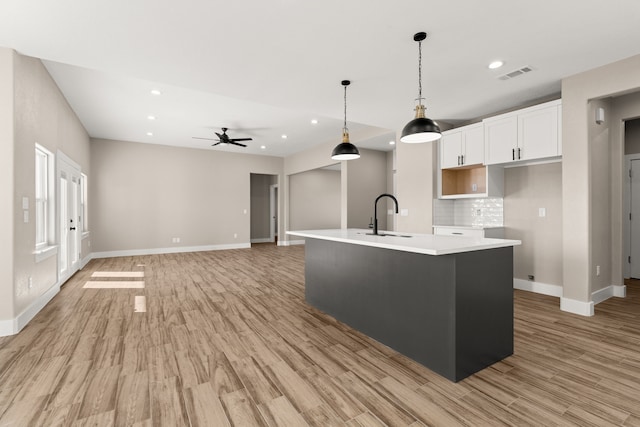 kitchen featuring pendant lighting, sink, white cabinetry, an island with sink, and light wood-type flooring