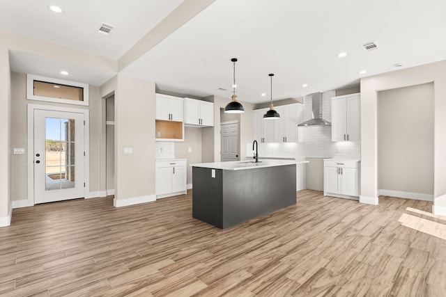 kitchen with pendant lighting, white cabinetry, sink, a kitchen island with sink, and wall chimney range hood