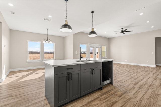 kitchen with pendant lighting, sink, gray cabinets, a kitchen island with sink, and light wood-type flooring