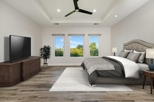 bedroom with ceiling fan, a tray ceiling, and light hardwood / wood-style flooring