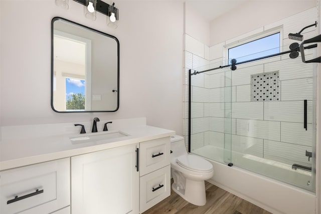 full bathroom featuring hardwood / wood-style flooring, vanity, shower / bath combination with glass door, and toilet