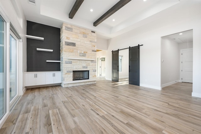 unfurnished living room featuring beamed ceiling, a fireplace, a barn door, and light wood-type flooring