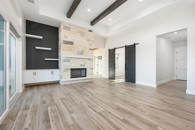 104 Cactus Cor, Horseshoe Bay, TX 78657 - unfurnished living room featuring beamed ceiling, a barn door, light wood finished floors, baseboards, and a stone fireplace
