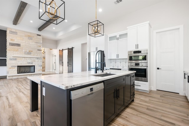 kitchen featuring sink, stainless steel appliances, an island with sink, white cabinets, and a barn door