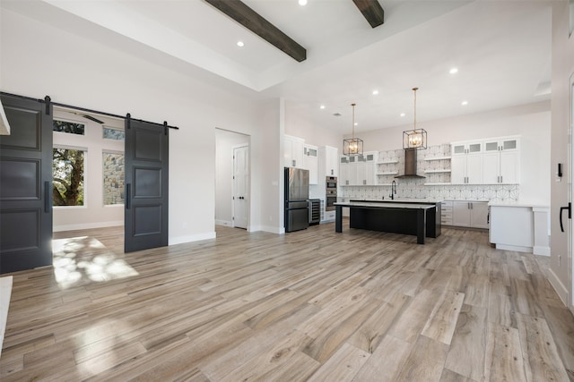 unfurnished living room featuring a towering ceiling, a barn door, beamed ceiling, and light wood-type flooring