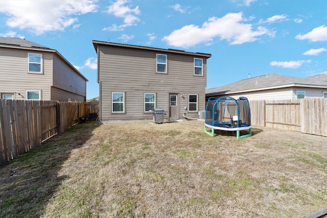 back of house with a trampoline and a lawn