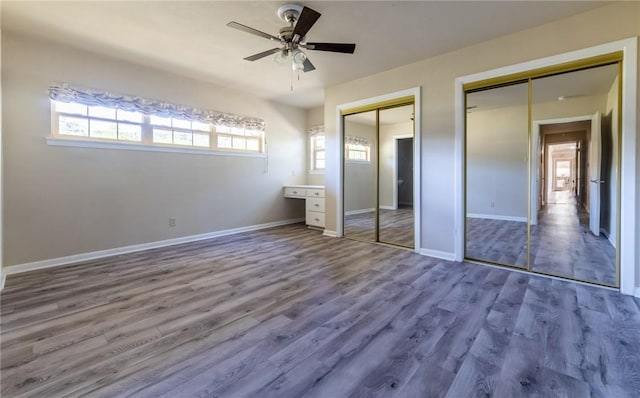 unfurnished bedroom with hardwood / wood-style floors, two closets, and ceiling fan