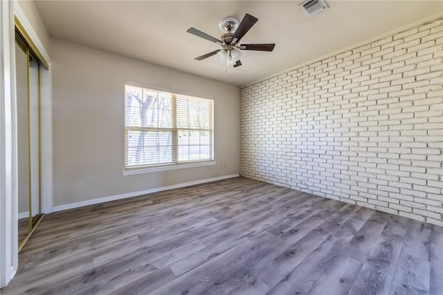 unfurnished bedroom with ceiling fan, brick wall, hardwood / wood-style floors, and a closet