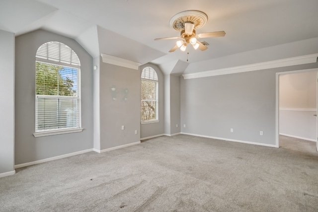 empty room with vaulted ceiling, ceiling fan, baseboards, and light colored carpet