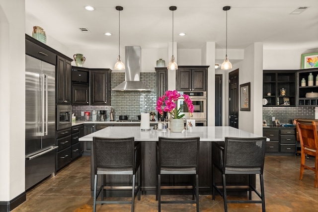 kitchen with tasteful backsplash, built in appliances, a center island with sink, pendant lighting, and exhaust hood