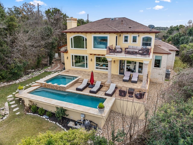 back of property featuring a patio, a balcony, and an in ground hot tub