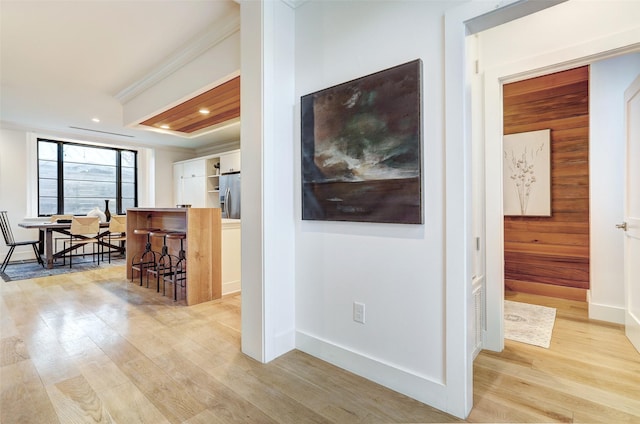 hallway featuring crown molding, wood walls, and light wood-type flooring