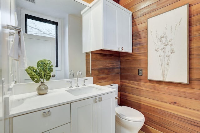 bathroom featuring vanity, toilet, and wood walls