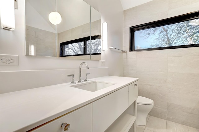 bathroom featuring lofted ceiling, toilet, tile walls, vanity, and tile patterned flooring