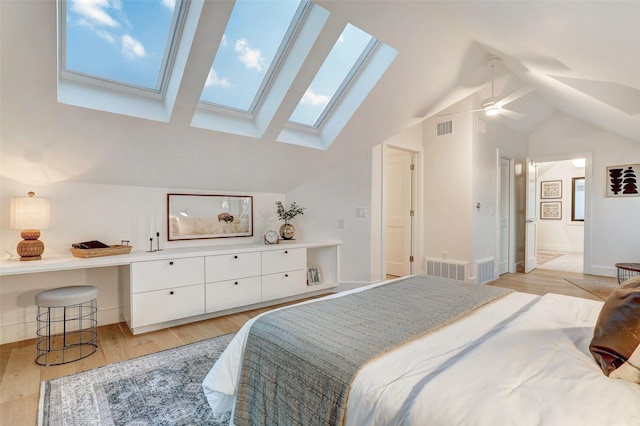 bedroom featuring ceiling fan, vaulted ceiling with skylight, light hardwood / wood-style floors, and ensuite bath