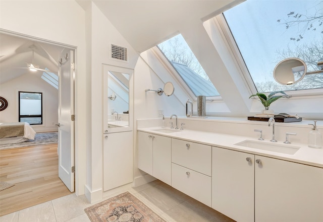 bathroom with tile patterned flooring, lofted ceiling with skylight, vanity, and ceiling fan