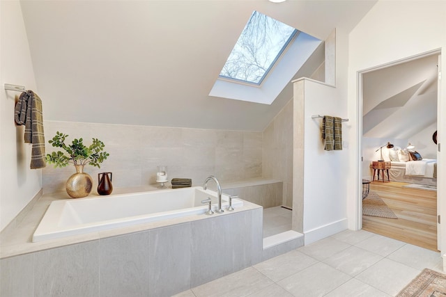 bathroom with tile patterned floors, lofted ceiling with skylight, and tiled tub