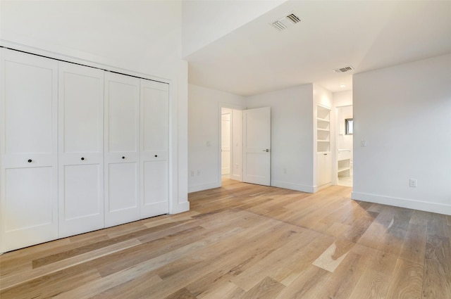 unfurnished bedroom with ensuite bathroom, light wood-type flooring, and a closet