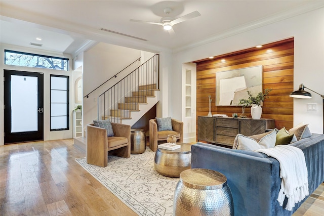 living room with crown molding, light hardwood / wood-style flooring, ceiling fan, wooden walls, and built in shelves