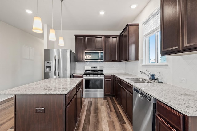 kitchen with sink, dark wood-type flooring, stainless steel appliances, a center island, and decorative light fixtures