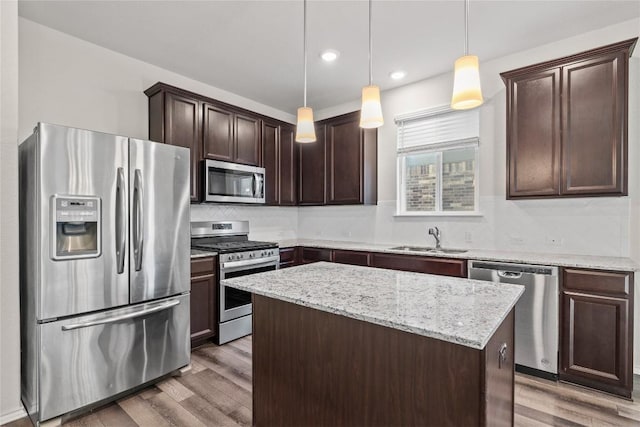 118 Grace Lilly Dr, Buda, TX 78610 - kitchen featuring appliances with stainless steel finishes, dark brown cabinetry, light wood-style floors, a kitchen island, and light stone countertops