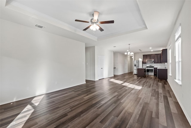 unfurnished living room with sink, ornamental molding, dark hardwood / wood-style floors, a tray ceiling, and ceiling fan with notable chandelier